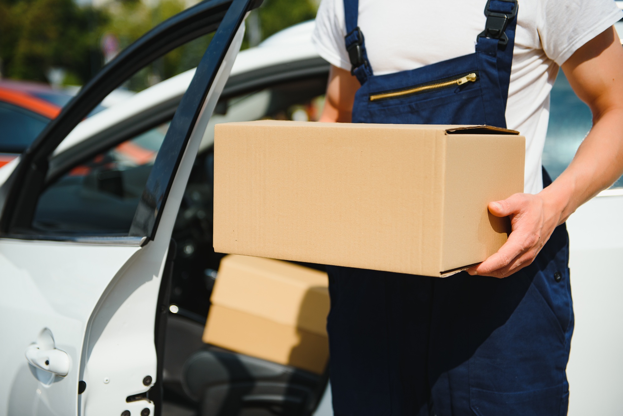 Deliveryman holds parcels at the car, delivering